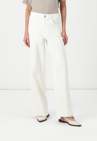 White wide-leg jeans made of denim, featuring a high waist, four pockets, and a clean finish. Paired with light-colored flat shoes.