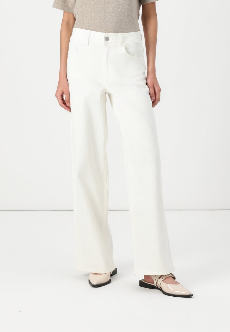 White wide-leg jeans made of denim, featuring a high waist, four pockets, and a clean finish. Paired with light-colored flat shoes.