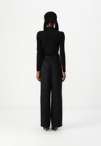 Haut noir à manches longues et pantalon large taille haute avec un motif texturé noir. L'ensemble présente une silhouette ajustée et un design minimaliste.