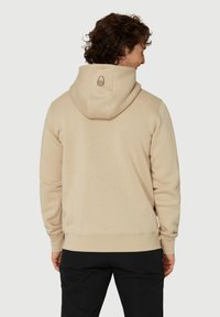 Sudadera beige con capucha ajustable, que presenta un pequeño gráfico en la parte trasera. Hecha de material suave, tiene un corte relajado y puños acanalados.