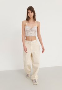 Cvećasti crop top s tankim naramenicama i nabranim detaljima, uparen s visokim, širokim hlačama krem boje i svijetlim tenisicama.