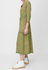 Grön blomsterklänning med trekvartslånga ärmar, lagerdesign, volang i nederkant, i kombination med vita högstövlar med genomskinlig sula.