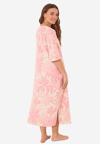 Maxi abito realizzato in tessuto leggero, con un motivo floreale rosa su uno sfondo crema, dotato di maniche corte e uno spacco laterale.