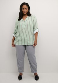 Light green collared blouse with vertical white and gray stripes, rolled sleeves, paired with gray trousers and black pointed-toe shoes.