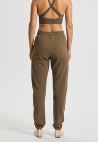 Olivgrüne sportliche Jogginghose mit elastischem Bund und Bündchen, kombiniert mit einem passenden rückenfreien Sport-BH mit gekreuzten Trägern.