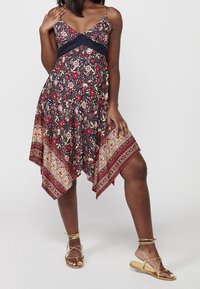 Robe maxi florale marine à fleurs rouges, accentuée par un ourlet à motifs. Dispose d'un bustier ajusté et de bretelles spaghetti réglables.