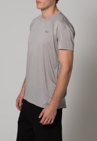 Ljust grå t-shirt med kort ärm, tillverkad av mjukt material, med en enkel rundad halsringning och en liten logotyp på övre vänstra bröstet.