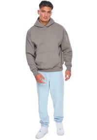Hættetrøje i dæmpet grå bomuldsblanding med forlommer, ribbede manchetter og kant. Båret med lyseblå jeans og hvide sneakers.