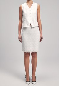 White, textured sleeveless top with a V-neck and buttons, paired with a white pencil skirt featuring a scalloped hem and similar pattern.