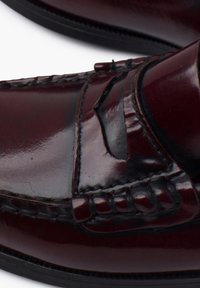 Burgundy leather loafers featuring a smooth finish, stitched detailing, raised accents, and a rubber sole for durability.