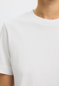 Valge puuvillane T-särk ümarate krae ja lühikeste varrukatega. Sile tekstuur, ilma nähtavate mustrite või logodeta. Lihtne ja klassikaline disain.