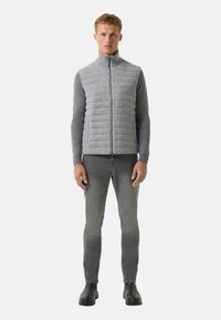 Hellegrau gesteppte Weste mit hohem Kragen, kombiniert mit einem dunkelgrauen Langarmshirt, grauen Jeans und schwarzen Stiefeletten.