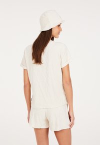 Witte katoenen set bestaande uit een T-shirt met korte mouwen en shorts, beide met een gestructureerd ruitpatroon. De bijpassende bucket hat maakt de look compleet.