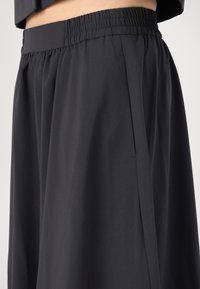 Pantalones negros de pierna ancha con cinturilla elástica, textura suave, detalle de bolsillo lateral y caída fluida.