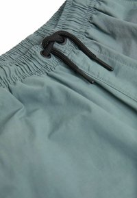 Shorts de bain bleu-vert clair avec une taille élastique, dotés d'un cordon noir pour ajustement et d'une texture de tissu lisse.