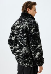 Zwart-wit gestreepte fleece jas met hoge kraag, oversized pasvorm en textuurstof. Kenmerkt losse mouwen en een afgeronde zoom.