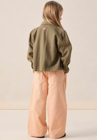 Veste vert olive avec une broderie en forme de cœur rose au dos, assortie à un pantalon large couleur pêche en tissu doux et texturé.