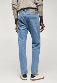 Vaqueros de mezclilla azul claro con un corte holgado, que cuentan con bolsillos traseros y una etiqueta marrón en la cintura. Llevados con zapatillas blancas y azul marino.