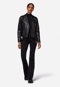 Schwarze Leder-Bikerjacke mit Reißverschlusstaschen, Druckknöpfen und einem leicht verkürzten Schnitt, kombiniert mit angepassten schwarzen Jeans und schwarzen Schuhen.