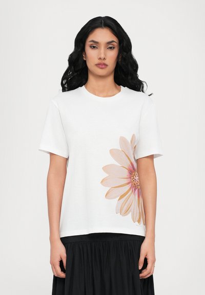 White cotton t-shirt featuring a large pink daisy graphic on the left side. Short sleeves, round neckline, and standard fit.