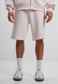 Lyserøde bomullsblandingsshorts med en afslappet pasform, har opfoldede kanter og et subtilt brandlogo på venstre lår. Bæres med hvide sokker og sneakers.