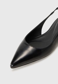 Sandal de salto em couro preto com bico fino e textura suave. Apresenta um vamp baixo e uma tira delicada no calcanhar.
