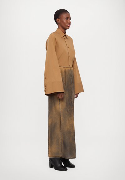 Brun knappad skjorta med vida ärmar, tillsammans med en lång, rostig beige kjol. Svarta klackstövlar kompletterar outfiten.
