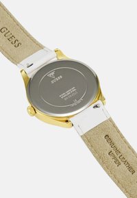 Gouden horloge met een roestvrijstalen kast en een witte lederen band. De achterkant heeft een merkaanduiding en waterdichte details.