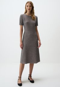 Robe grise et bordeaux midi avec des manches courtes, motif en damier texturé, encolure ronde et silhouette ajustée. Ballets noirs avec des brides autour de la cheville.