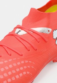 Φωτεινό κόκκινο παπούτσι ποδοσφαίρου με υφή στο πάνω μέρος, λευκές λεπτομέρειες και εφαρμοστό γιακά με περίτεχνο κορδόνι.