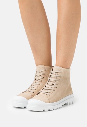 Zapatillas altas de gamuza beige con suelas de goma blanca, que presentan punteras redondeadas, diseño de cordones y paneles texturizados.