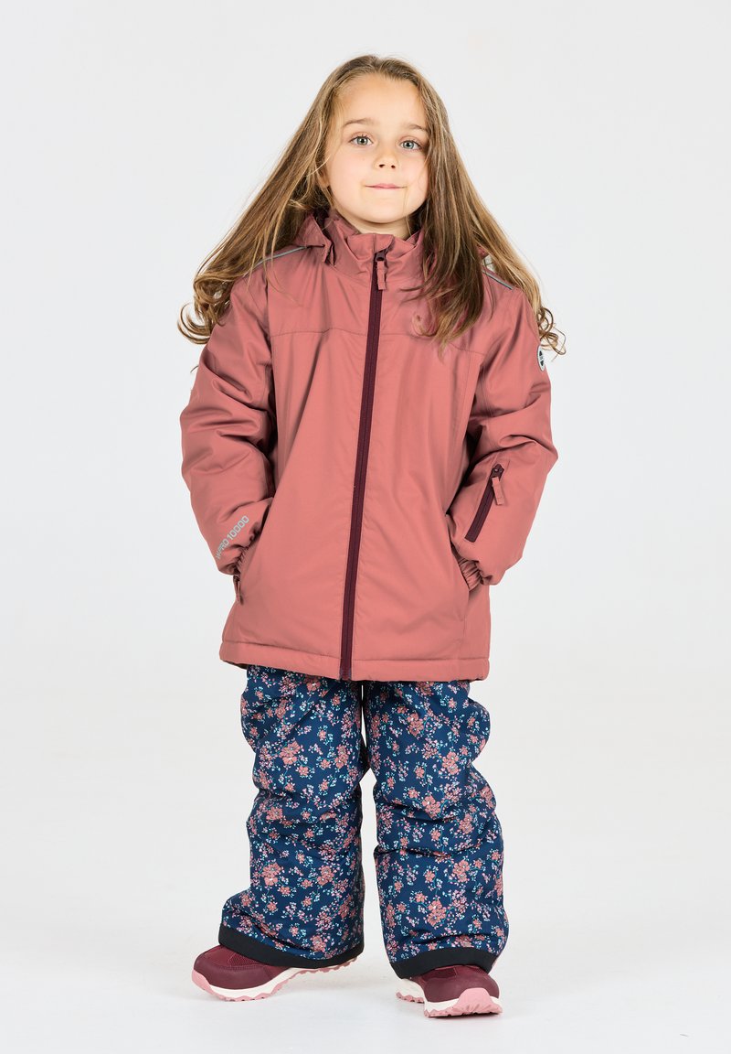 Rosa isolierte Jacke mit einem vorderen Reißverschluss, kombiniert mit navyblauen Schneehosen mit floralem Muster. Beide Teile haben einen entspannten Schnitt und eine warme Textur.