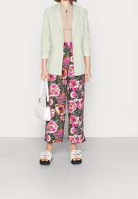 Světle zelený blejzr, béžový top se zipem na krku, květinové široké kalhoty v růžové a zelené, bílá taška a chunky bílé sandály se zapínáním.