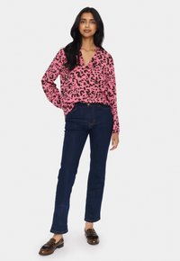Rosa leopardmönstrad blus med V-hals och långa ärmar, tillsammans med mörkblå rakbeniga jeans och bruna loafers.