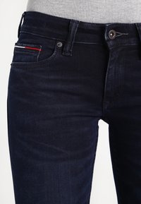 Mörkblå denimjeans med smal passform, som har framfickor, en diskret röd detalj på fickfodret och klassiska metalldetaljer.