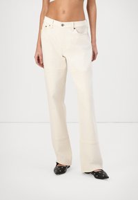 White high-waisted denim flared pants with side seam accents and subtle stitching details. Worn with black pointed-toe flats.