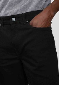 Jean en denim noir au design ajusté, avec une poche avant, fermeture à bouton en métal et texture subtile.