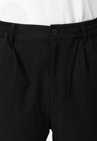 Black trousers with a smooth texture, featuring an elastic waistband, button closure, and side pockets. Simple and functional design.