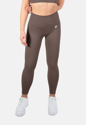 Braune Sportleggings mit hohem Bund, geripptem Muster und kleinem Logo auf dem Oberschenkel, kombiniert mit weißen Sneakers.