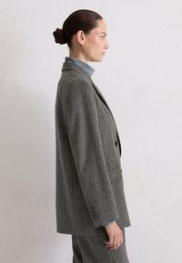 Grijze geruite blazer met een slim fit, geknipsde revers en twee knopen. Gecombineerd met een lichtblauwe coltrui. Soepele textuur, gestructureerd ontwerp.