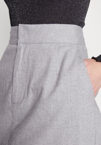 Pantalons gris ajustés avec une texture lisse, taille haute, poches latérales et un léger motif en chevron.