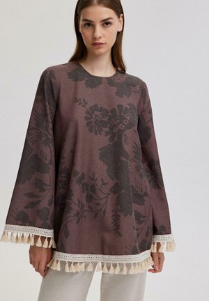 Brown floral print top with long bell sleeves, lace trim, and tassel accents along the hem and sleeves. Soft texture, relaxed fit.