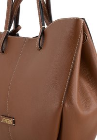Brown leather tote bag with white stitching and dual handles, featuring a small "VENEZIA" label in gold lettering on the front side.