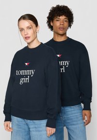 Marineblå sweatshirts lavet af en bomuldsblanding; indeholder hvid "tommy girl" tekst og broderet stjernes design med røde og hvide detaljer.