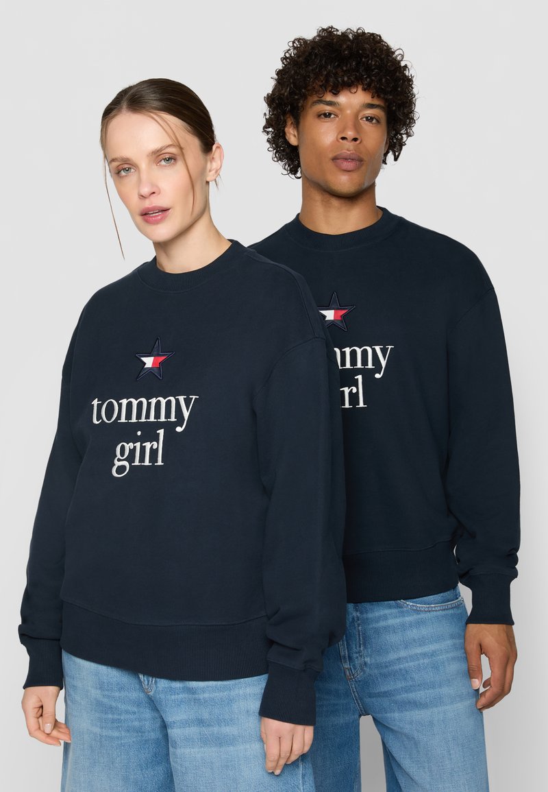 Marineblå sweatshirts lavet af en bomuldsblanding; indeholder hvid "tommy girl" tekst og broderet stjernes design med røde og hvide detaljer.
