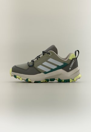 Niedriger Adidas Terrex Wanderschuh in Grün und Grau mit gelber und dunkelgrüner profilierter Sohle, weißen Streifen und Zuglasche an der Ferse.