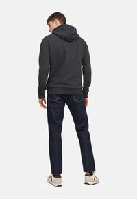 Dunkelgrauer Hoodie mit Kapuze und gerippten Bündchen, kombiniert mit dunklen Jeans und weißen Sneakern mit roten Akzenten. Schlichte, lässige Gestaltung.