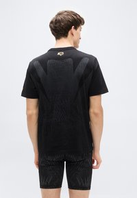 Μα ύρο μπλουζάκι με υφή στο πίσω μέρος, κοντά μανίκια και χρυσό λογότυπο στο λαιμό. Φορεμένο με μαύρο σορτς.