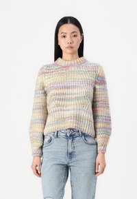 Pull en tricot multicolore avec une texture côtelée, un col rond et des manches longues. Associé à un jean taille haute bleu clair.