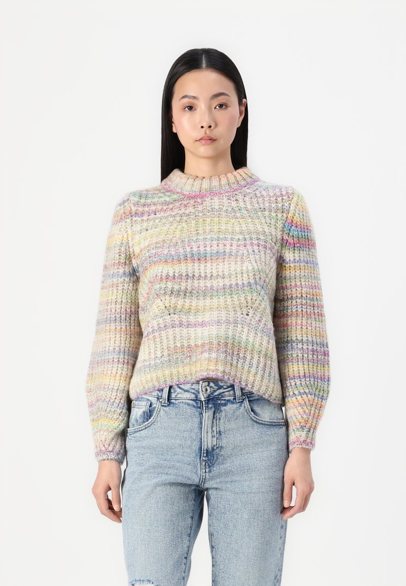 Pull en tricot multicolore avec une texture côtelée, un col rond et des manches longues. Associé à un jean taille haute bleu clair.